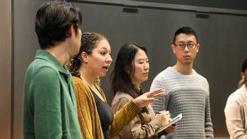 A group of students stand, discuss and take notes